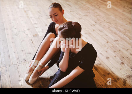 Due ballerine parlando e sorridente seduto su un pavimento di legno Foto Stock
