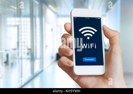 Close-up della mano che tiene lo smartphone con il simbolo wifi e collegare il pulsante sullo schermo per l'accesso pubblico a internet wireless, offuscata building interior Foto Stock