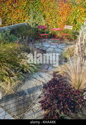 Piccolo giardino patio con pavimentazione in lastre, tavolo da pranzo e sedie e Colore di autunno piante fogliame, England, Regno Unito Foto Stock