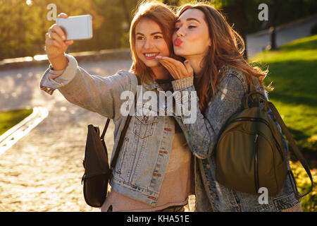 Due sorridente amici di sesso femminile in abbigliamento casual rendendo selfie sullo smartphone, per esterno Foto Stock