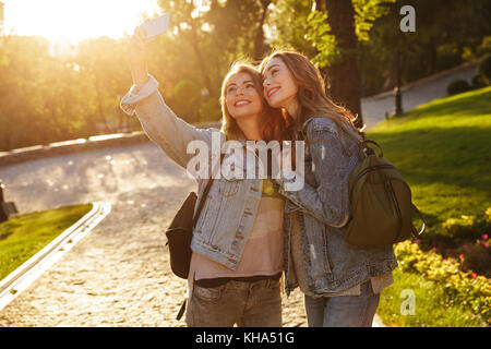 Due attraenti caucasian donna in abbigliamento casual rendendo selfie sullo smartphone, per esterno Foto Stock