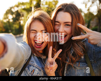 Due giovani felici brunette donna avendo divertimento tenendo selfie sul telefono cellulare, per esterno Foto Stock