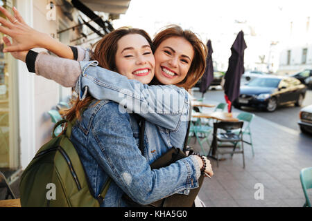 Due giovani felici brunette ragazze che abbraccia ogni altra, guardando la telecamera, città outdoor Foto Stock