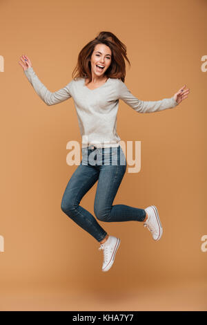 Lunghezza completa di foto affascinante giovane donna in abbigliamento casual saltando su sfondo beige Foto Stock