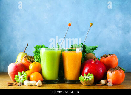 Appena miscelato frullati di frutta di vari colori e sapori in vetro nel vassoio di legno giallo, verde. sul tavolo di legno e sfondo blu Foto Stock