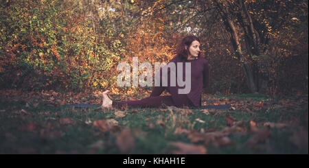 Ragazza di una giornata autunnale a praticare yoga all'aperto, facendo ardha matsyendrasana (metà signore dei pesci, vakrasana o mezza torsione spinale), bracci sul retro Foto Stock