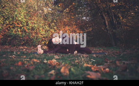 Ragazza di una luminosa giornata autunnale a praticare yoga all'aperto, facendo parivrtta janu sirsasana (giravano testa a ginocchio) pongono, con un braccio dietro la schiena Foto Stock