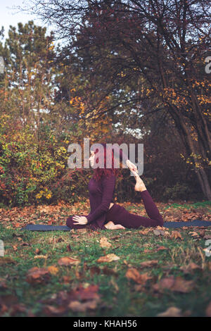 Ragazza di una luminosa giornata autunnale a praticare yoga all'aperto, facendo una variazione su uno zampe piccioni King (eka pada rajakapotasana) Foto Stock