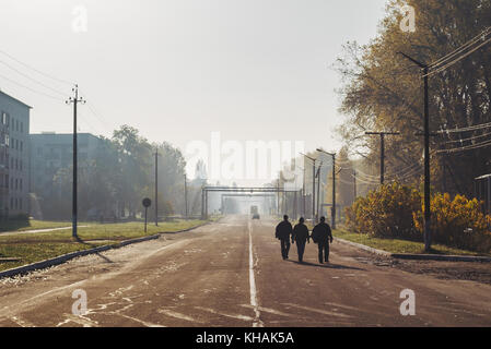 Tre uomini a piedi giù per la strada una mattina al lavoro di Chernobyl, in Ucraina Foto Stock