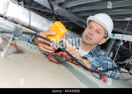 Elettricista di ispezionare i fili morto sul soffitto alto Foto Stock