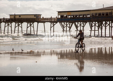 Ciclista sulla spiaggia nei pressi del molo con riflessioni. Foto Stock