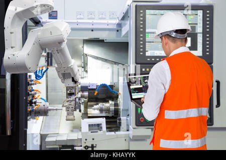 Ingegnere utilizzando computer portatili per la manutenzione automatica del braccio robotico con macchina CNC in smart factory. industria 4.0 concetto Foto Stock