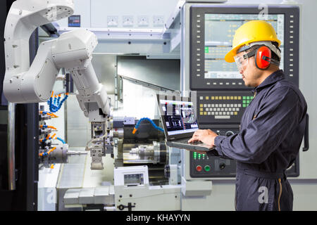 Tecnico di manutenzione utilizzando il computer portatile il controllo automatico di mano robotica con macchina CNC in smart factory. industria 4.0 concetto Foto Stock
