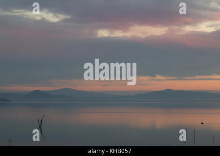 Un lago al tramonto, con bellissime tonalità calde nel cielo e acqua e alcuni poli in primo piano Foto Stock