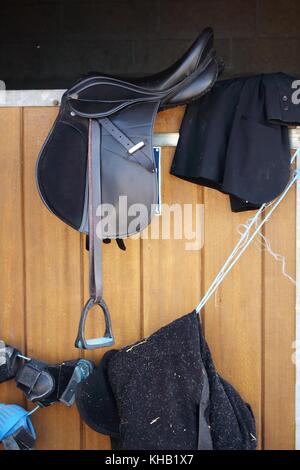 Una sella di cavallo e vari accessori collocati sul bordo della porta della stalla Foto Stock