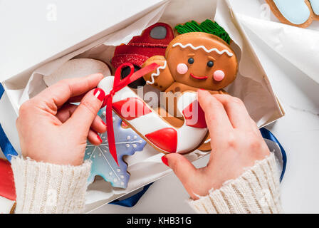 Preparazione per il natale, la decorazione tradizionale di pan di zenzero con zucchero multicolore smalto, la ragazza si ripiega i biscotti in una scatola regalo bianca, con nastro Foto Stock