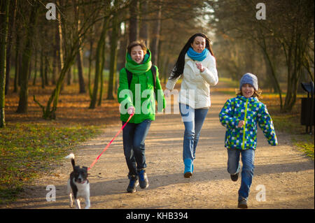 Madre e due figli divertendosi in autunno park. insieme essi stanno camminando in bianco e nero cute cane. famiglia con risate, in esecuzione per il pet. Foto Stock