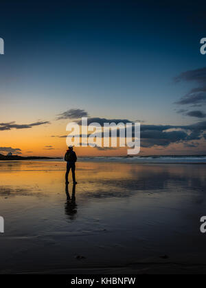 Uomo in piedi sulla spiaggia al tramonto Foto Stock