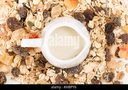 Bianco latte pentola con latte vegetale, sulla pila di muesli con frutta secca, closeup sfondo. Foto Stock