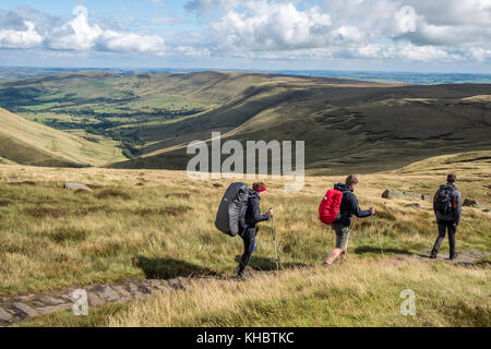 Walkers su un sentiero brughiera nel Peak District campagna con la valle di Edale a distanza. Kinder Scout, Derbyshire, England, Regno Unito Foto Stock