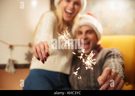 Felice coppia giovane in Santa's hat holding botti, messa a fuoco selettiva delle luci Foto Stock