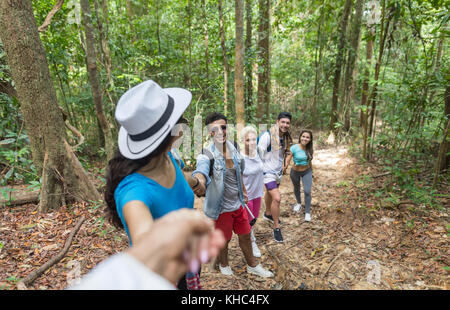 Gruppo di persone con zaini trekking sul Sentiero forestale holding hands aiutando, mix gara giovani uomini e una donna sulla passeggiata di turisti Foto Stock