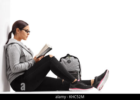 Femmina studente adolescente leggendo un libro e poggiante contro una parete isolata su sfondo bianco Foto Stock