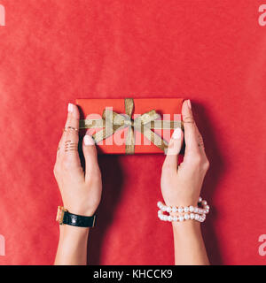 Confezione regalo rossa con nastro d'oro in mani femminili vista superiore Foto Stock
