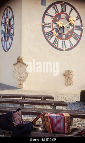 Una vecchia fisarmonica austriaco sulla panca in legno nella parte anteriore di una grande città orologio, città di Graz in Austria. Foto Stock