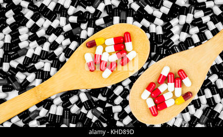 Colorato di antibiotici pillole di capsule in cucchiaio di legno sul nero e sfondo bianco di capsule. La resistenza al farmaco concetto. antibiotici uso di droga con re Foto Stock