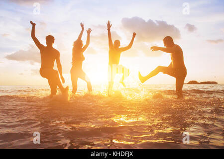 La folla di amici divertendosi in acqua al tramonto, sagome di persone contente e godendo le vacanze estive Foto Stock