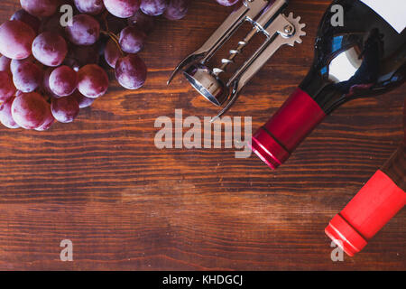 Sfondo di vino, vista dall'alto di due bottiglie, cavatappi e uva scuro sulla scrivania in legno Foto Stock