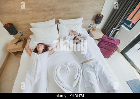 Coppia felice in camera di questo hotel di lusso, vacanze viaggio alloggi, vista dall'alto di sorridere l uomo e la donna sdraiata sul letto Foto Stock