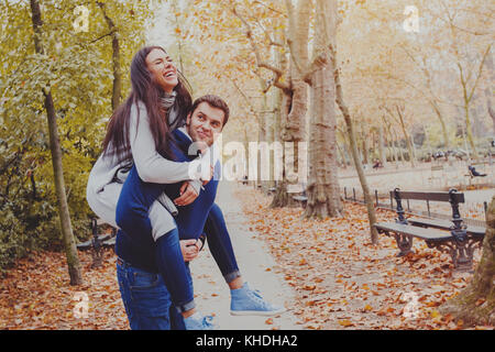 Uomo Donna portante piggyback, incontri, coppia giovane ridere in autunno park Foto Stock