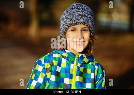 Ritratto di un sorridente ragazzo di 9-10 anni. Il ragazzo è vestito con una camicia colorata e un cappuccio a maglia. Foto Stock