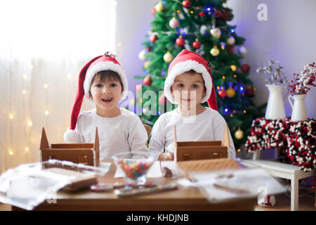 Due ragazzi dolce, fratelli, rendendo gingerbread cookies house, la decorazione a casa nella parte anteriore dell'albero di Natale, bambini che giocano e godendo di Natale c Foto Stock