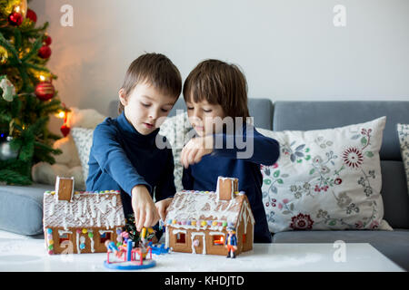 Due bambini, ragazzo fratelli, giocando con Gingerbread case e un po' di giocattoli a casa per Natale Foto Stock