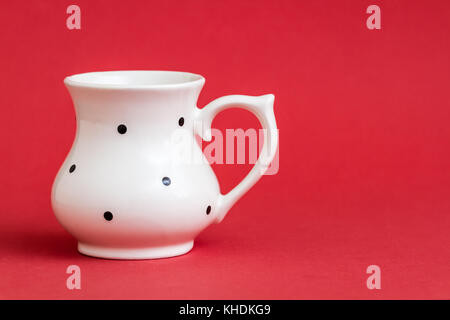 Close up white vintage tazza di siero di latte con un puntino nero pattern su sfondo rosso Foto Stock