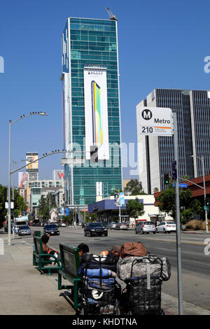 Persone senza dimora seduto su una fermata bus da banco e la vista del tramonto Vine Tower con Apple iPhone X annuncio a Hollywood, LA KATHY DEWITT Foto Stock