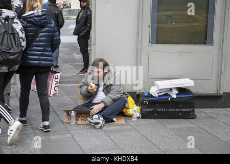 L'uomo senza casa si siede sul marciapiede chiedendo aiuto mentre mangia una mela nel centro di Manhattan, New York City Foto Stock