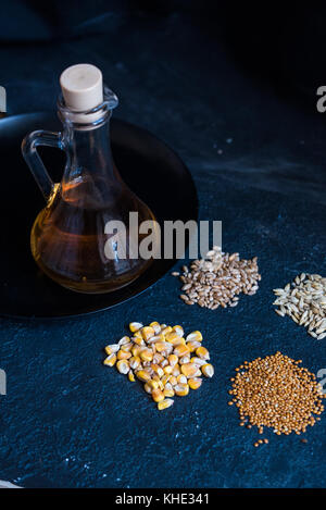 Pile di quattro diversi cereali e olio nel decanter Foto Stock