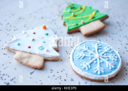 Due gingerbread cookies a forma di alberi di Natale e un cookie nella forma di un tondo blu il simbolo del fiocco di neve su un tavolo in legno e sparse chia Foto Stock