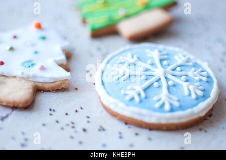 Due gingerbread cookies a forma di alberi di Natale e un cookie nella forma di un tondo blu il simbolo del fiocco di neve su un tavolo in legno e sparse chia Foto Stock