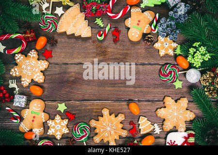 Il natale di panpepato biscotti fatti in casa su un tavolo di legno con canditi, albero di natale rami e Nuovo Anno decorazioni. xmas sfondo del telaio Foto Stock