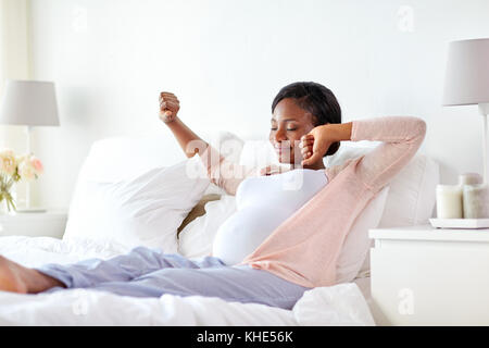 Felice donna africana incinta stretching nel letto Foto Stock