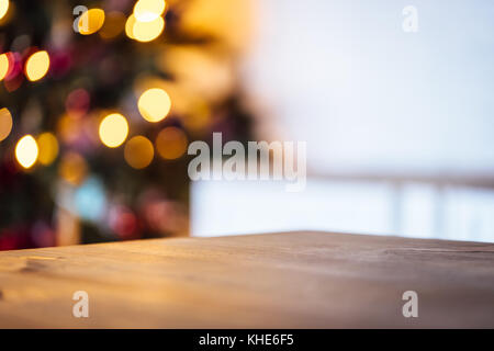 Vacanze di Natale sfondo con vuoto tavolo rustico e il bokeh di fondo del soggiorno con l'albero di natale sul secondo piano Foto Stock