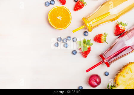 Il cibo sano con il rosso e il giallo frullati in bottiglie con cannucce e ingredienti: arancia, fragola, ananas, mirtilli e fragole su bianco w Foto Stock