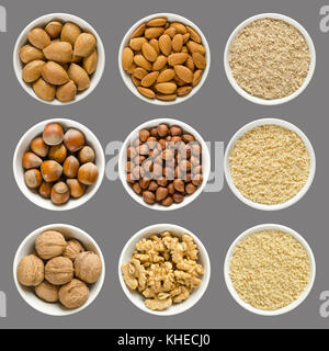 Mandorle, nocciole e noci in ciotole. interi, decorticati e dadi di messa a terra in porcellana bianca. Prunus dulcis, corylus avellana e Juglans regia. foto. Foto Stock