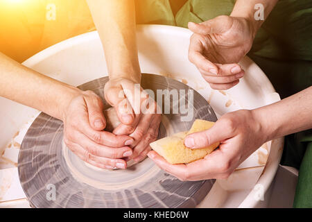 Un close-up della donna potter insegna l'allievo per effettuare correttamente una ciotola profonda di argilla sul tornio del vasaio in officina. formazione potter a lavorare Foto Stock