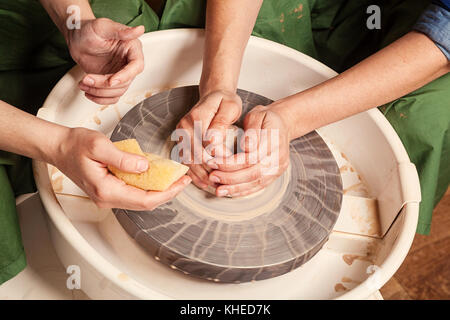 Un close-up della donna potter insegna l'allievo per effettuare correttamente una ciotola profonda di argilla sul tornio del vasaio in officina. formazione potter a lavorare Foto Stock